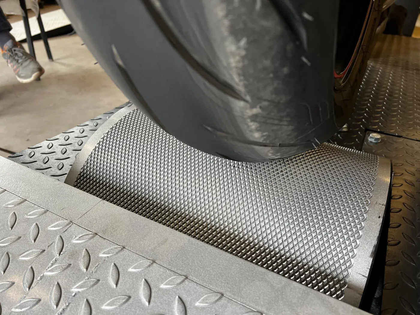 Primo piano di uno pneumatico per moto su un rullo del banco con superficie lavorata.